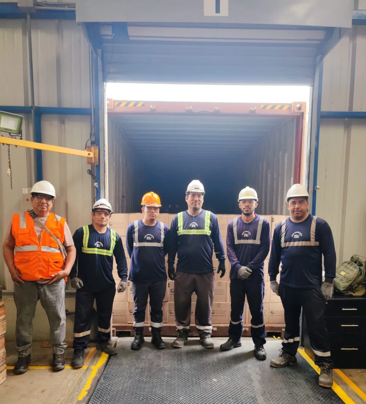 Cuadrilla uniformada de estibadores de Logística M&J con casco, lentes y chaleco frente a un contenedor en Lima